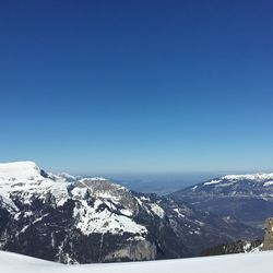 Scenic view of snow covered mountains against clear blue sky