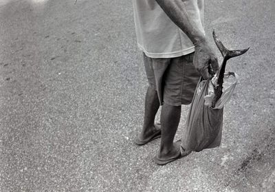 Low section of man holding fish in plastic bag on road