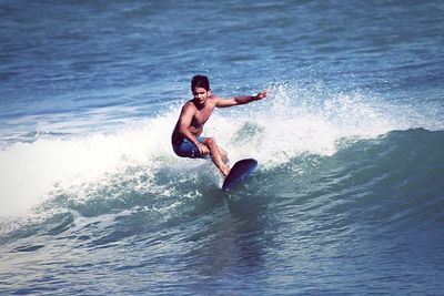 Shirtless man surfing in sea
