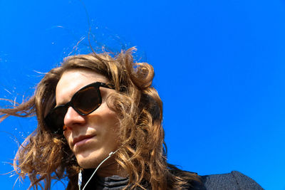 Low angle view of young woman against clear blue sky