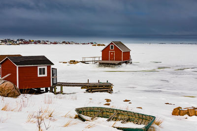 House on snow covered land by building against sky