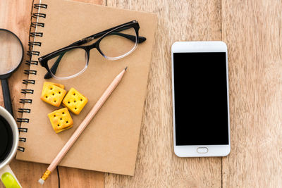 Directly above shot of mobile phone by eyeglasses and food on table