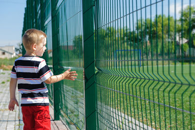 Rear view of boy looking through fence