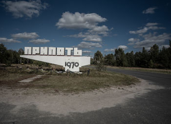 Road sign by street against sky in city