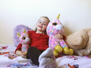 Portrait of girl with stuffed toys against wall on bed at home