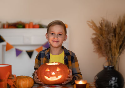 Portrait of smiling boy holding jack o lantern against wall