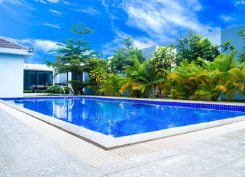 Swimming pool by trees against blue sky