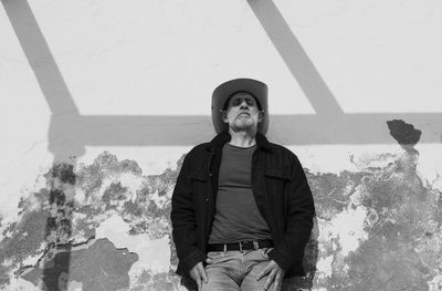 Portrait of adult man in cowboy hat and jeans against wall with sunlight and shadow. almeria, spain