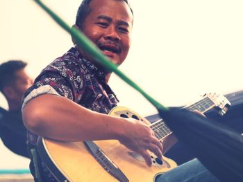 Portrait of mature man with acoustic guitar against sky