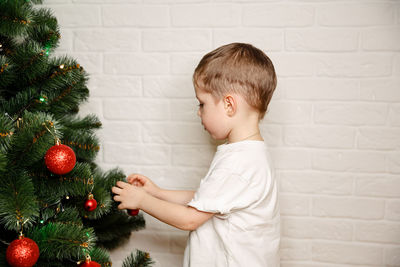 Boy decorating christmas tree against wall