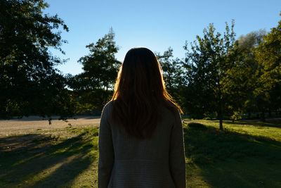 Rear view of woman standing by trees against sky