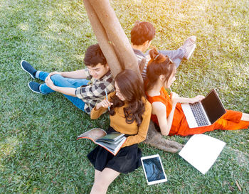 High angle view of friends studying while sitting by tree on field