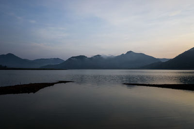 Scenic view of lake by mountains against sky during sunset