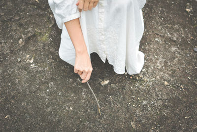 Cropped image of woman holding twig while crouching on field