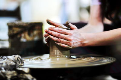 Midsection of woman shaping earthenware on pottery wheel