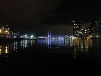 Illuminated city by sea against sky at night