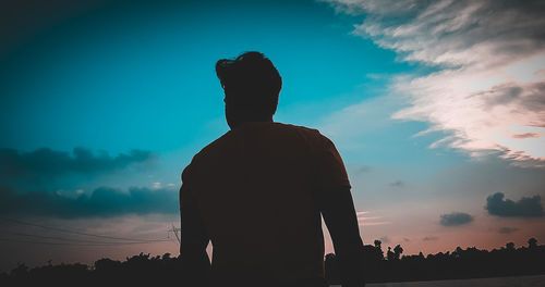 Rear view of silhouette man standing against sky at sunset