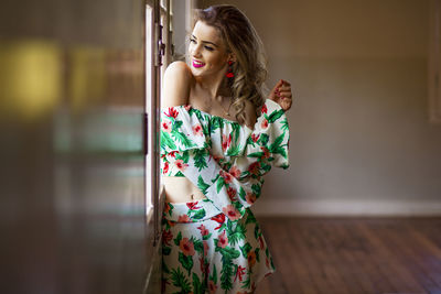 Smiling mid adult woman looking through window while standing against wall