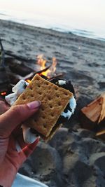 Cropped hand holding food over bonfire