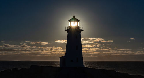 Lighthouse by sea against sky during sunset