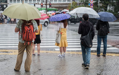 People holding umbrellas while standing on street during rainy season