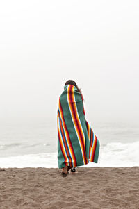 Rear view of woman wrapped in towel walking on shore at beach