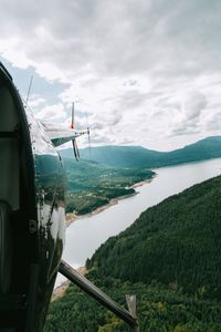 Cropped helicopter flying over lake and forest in cloudy sky