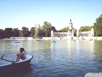 Woman relaxing on boats in lake at buen retiro park against clear sky