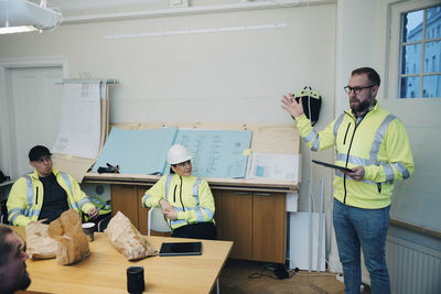 Male building contractor gesturing while discussing with colleagues in office