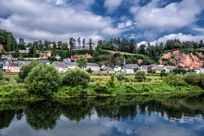 Scenic view of river by trees and buildings against sky