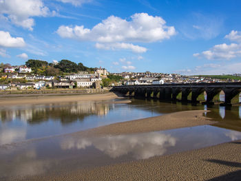 Bridge over river by buildings against sky