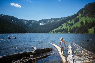 Girl walking on log in lake against blue sky at forest