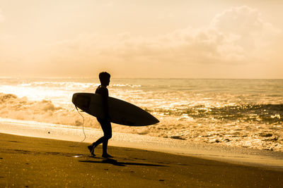 Silhouette man standing on beach against sky during sunset