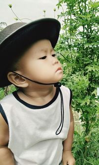 Cute boy looking away while standing against plants