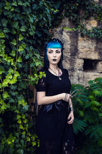 Beautiful goth girl with bright blue hair standing in the green ivy. on the eve of halloween