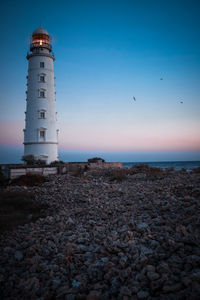 Lighthouse on beach by sea against sky during sunset