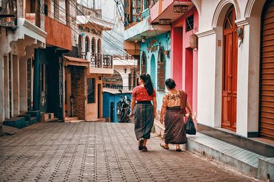 Rear view of women walking on street amidst buildings