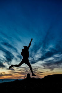 Rear view of silhouette woman standing on beach against sky during sunset