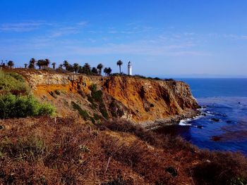 Scenic view of cliff by sea against blue sky