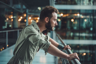 Side view of thoughtful handsome mid adult man looking away while standing by railing in building