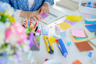 High angle view of woman holding multi colored pencils on table