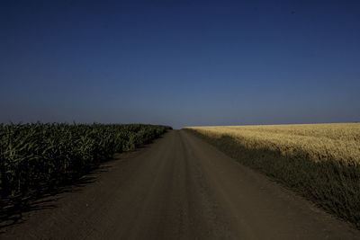 Road amidst field against clear sky