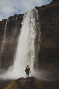 Rear view of woman standing on cliff against waterfall