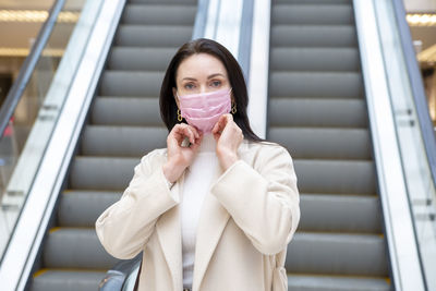 Portrait of woman wearing mask standing against escalator