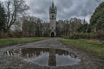 Reflection of building in puddle against cloudy sky