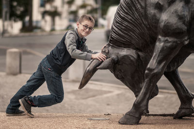 Smiling boy holding horns of bull statue by city street