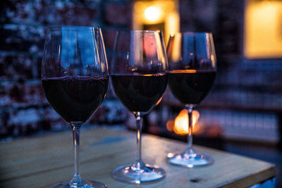 Three red wine glasses sitting on table with a brick wall and a glowing fire in the background