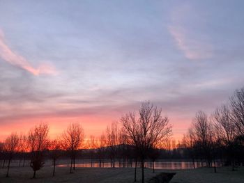 Bare trees on field against romantic sky at sunset