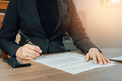 Midsection of businesswoman writing on document at office