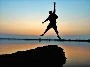 Silhouette man jumping on lake against sky during sunset